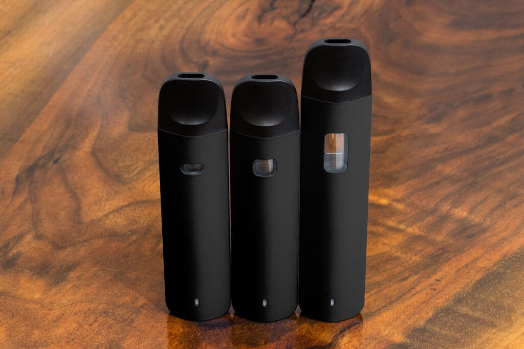 3 Traveler Extreme Glass CFB Pens in black are vertically standing side by side against a warm wood surface. The mouthpiece ends are at the top. The pen chamber size varies between the pens, starting with the shortest on the left to the tallest on the right to denote the different capacities available.