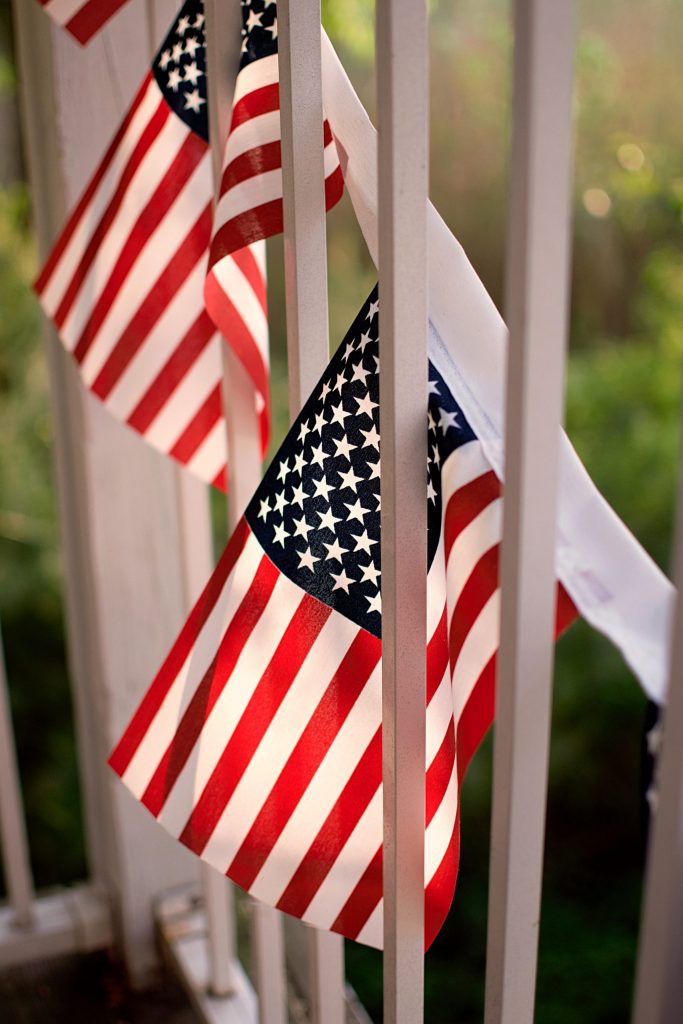 Patriotic American flags hanging decorations on white picket fence