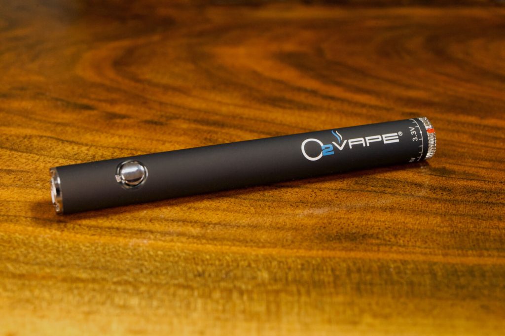 1 black Vari-Vape ® 510 Thread Battery is displayed horizontally against a warm wood surface. The O2VAPE logo is visible on the matte black body. There is a clear flat disc with a red indicator on one end.