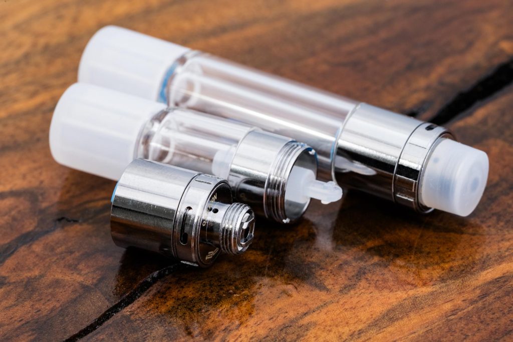 2 white All Glass Vari-Flow Vape Cartridges are displayed horizontally at an angle. The longer 1ml cartridge at the top and the shorter .5ml cartridge is beneath. The .5ml cartridge is open.