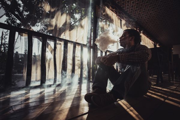 vaping young man produces vapor on sunset silhouette.