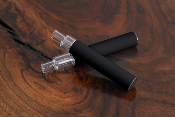 Diagonal arrangement of two unbranded black Traveler Extreme All Glass Bucket AIO devices crossed on a wood background, showcasing the all-glass mouthpiece and sleek matte body. Ideal for wholesale distribution.