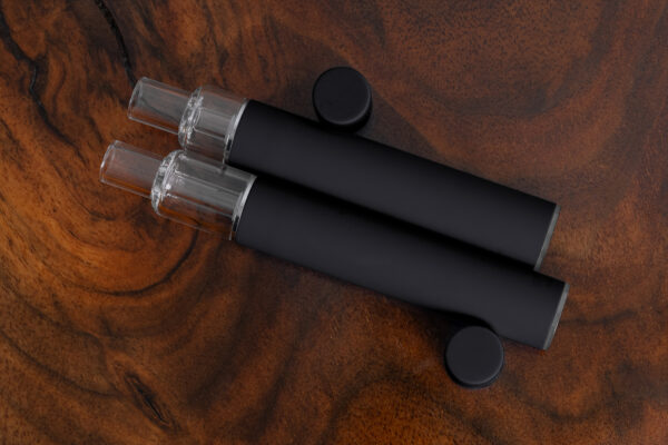 Side view of two black unbranded Traveler Extreme All Glass Bucket AIO vape pens with fully transparent tanks and matte black barrels. Clean design tailored for bulk purchase and private label.