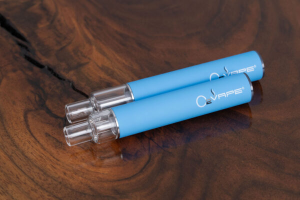 Top-down view of two O2VAPE Traveler Extreme All Glass Bucket AIO vape pens with matte blue finish and transparent all-glass tanks, resting on a natural wood surface. Highlights two different tank sizes in 0.5ml and 1ml.